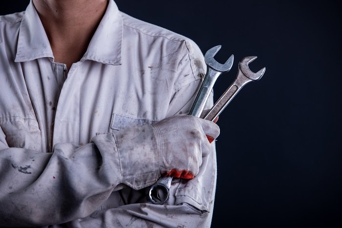Car mechanic wearing a white uniform stand holding wrench isolated on gray background with copy space.