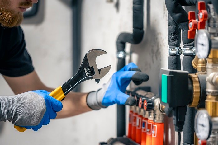 A man installs a heating system in a house and checks the pipes with a wrench. Adjusting heating valves in a residential building. A plumbing and heating technician works.